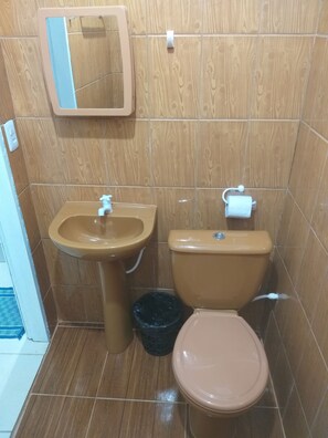 A bathroom with a wooden wall, a sink, a toilet, and a trash bin.