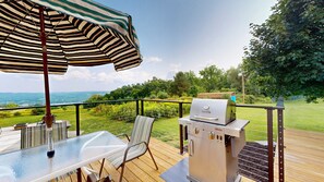 A deck with a glass table, striped umbrella, and a Char-Broil grill.