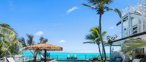 A pool area with lounge chairs, a thatched umbrella, and a view of the ocean.