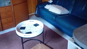 Una habitación acogedora con un sofá de cuero azul, una lámpara blanca, una mesita redonda y un mueble de madera.