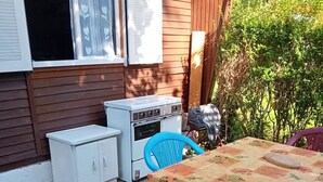 Un patio exterior con una mesa cubierta con un mantel floral, una silla azul y un horno blanco.