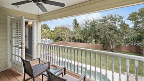 A covered porch with a ceiling fan, a table with chairs, and a view of a backyard with a pool and trees. - Whispering Waves: Pool, Bikes & Walk to Beach (Melbourne Beach)