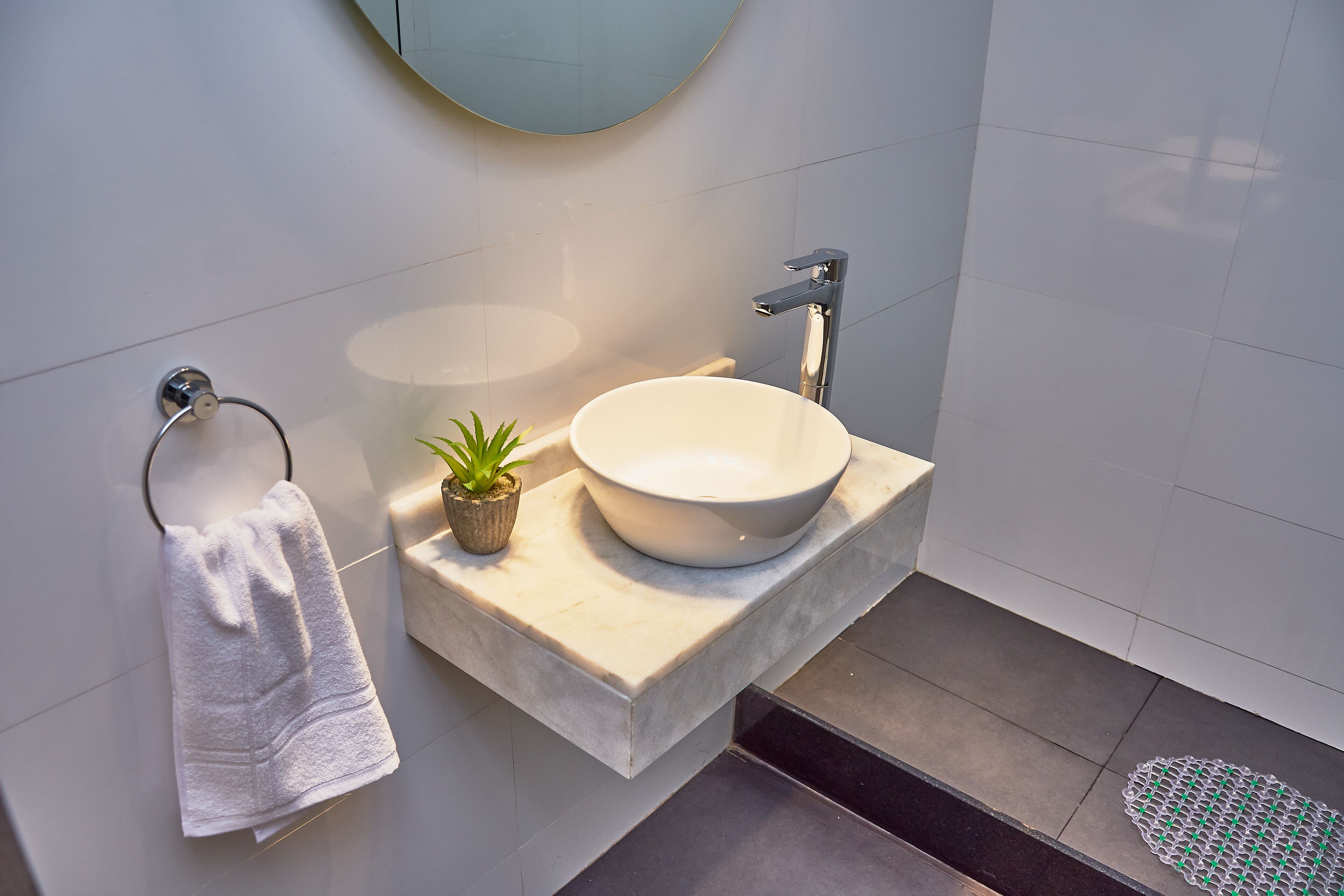 A modern bathroom with a white sink, a towel rack, and a small potted plant.