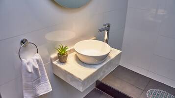 A modern bathroom with a white sink, a towel rack, and a small potted plant.