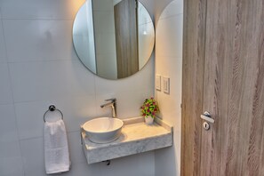 A bathroom with a white sink, a round mirror, a towel rack, and a wooden door. - Babel Campus (Buenos Aires)