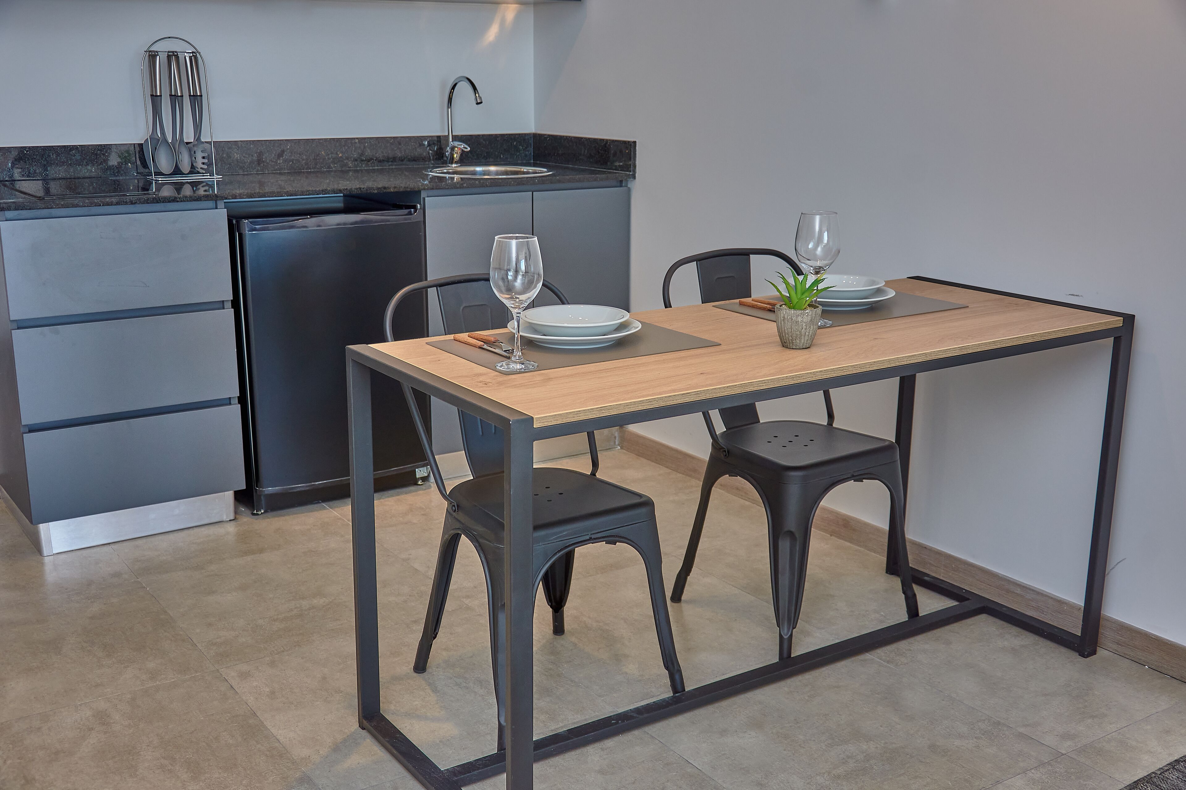 A compact kitchen with a built-in dishwasher, a sink, and a dining area with two stools and a table.