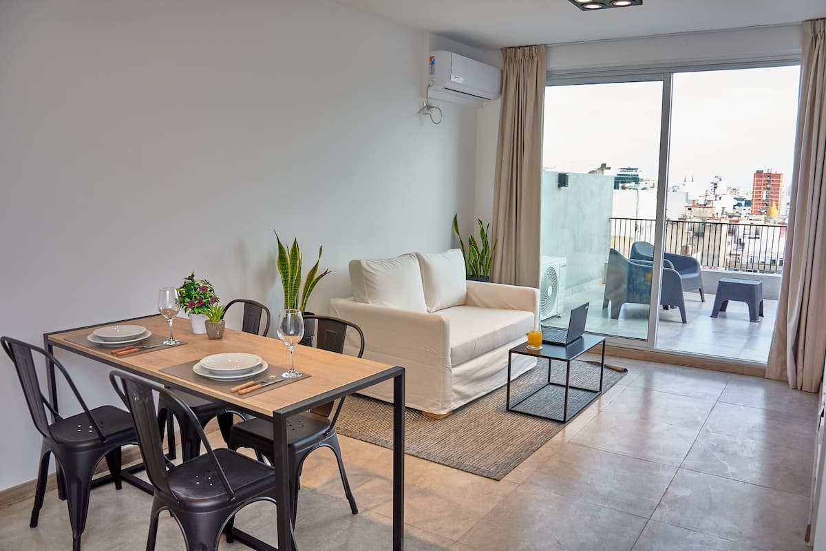 A modern living room with a dining area, a sofa, and a balcony with a city view.