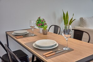 A dining table set with plates, cutlery, and a glass of water, accompanied by a small potted plant and a vase with a tall plant. - Babel Campus (Buenos Aires)