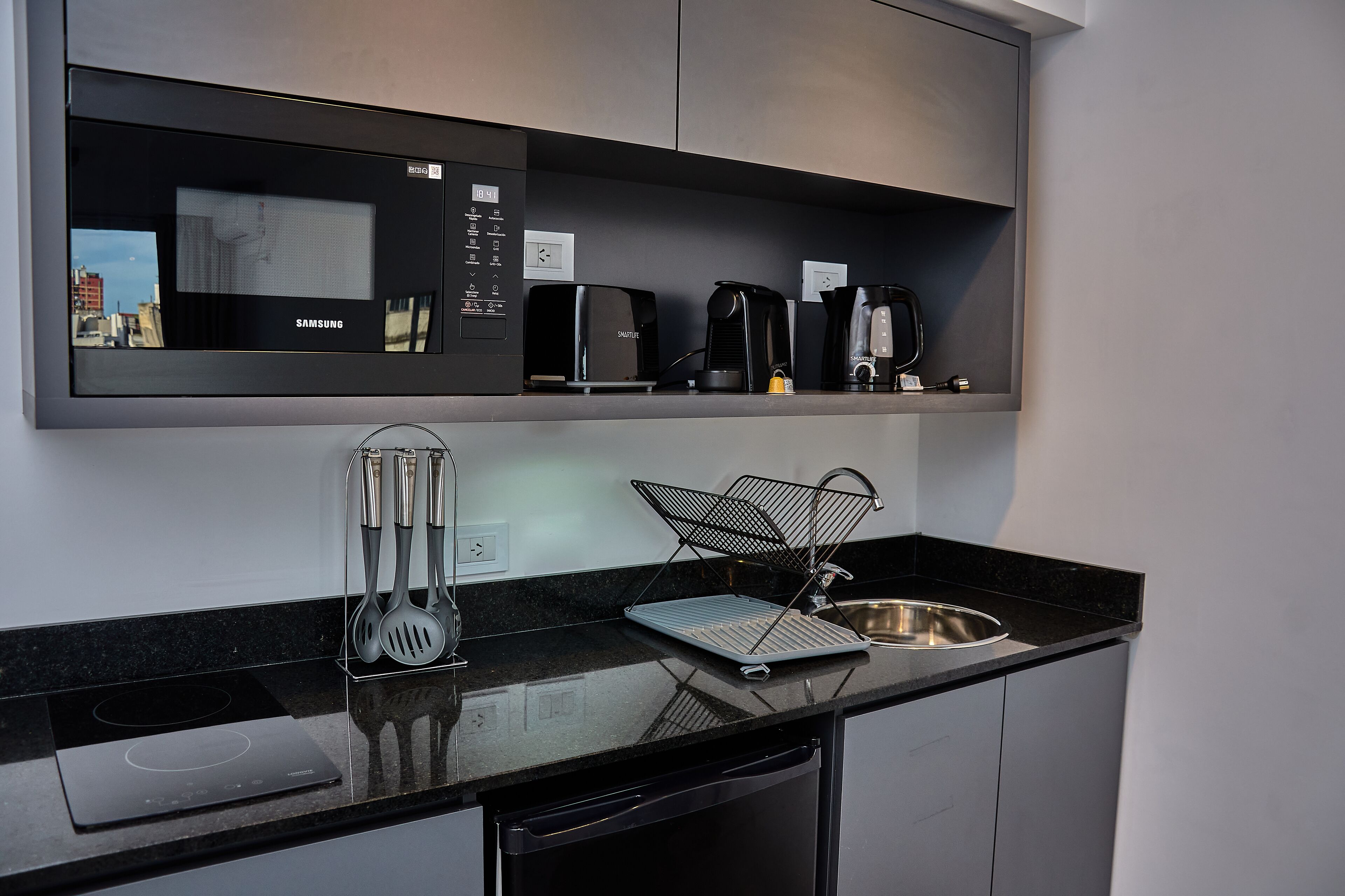 Een moderne keuken met een inbouwmagnetron, koffiezetapparaat en broodrooster. Er is een spoelbak en een afwasschaal op het aanrecht.