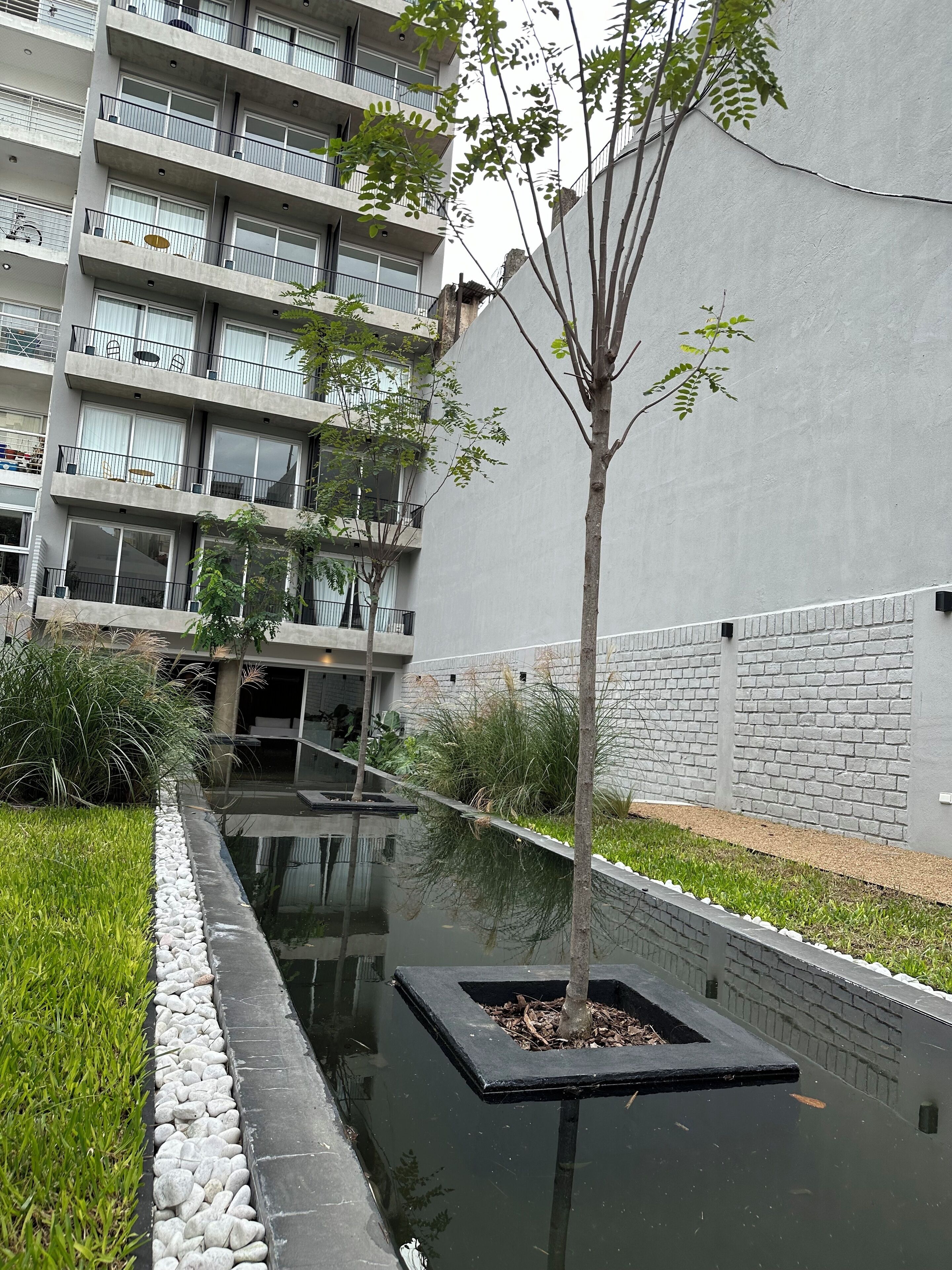 Un edificio de apartamentos moderno con varios balcones, un estrecho canal de agua y un pequeño árbol en una maceta.