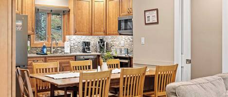A modern kitchen with wooden cabinets, a dining area with wooden chairs, and a built-in microwave.