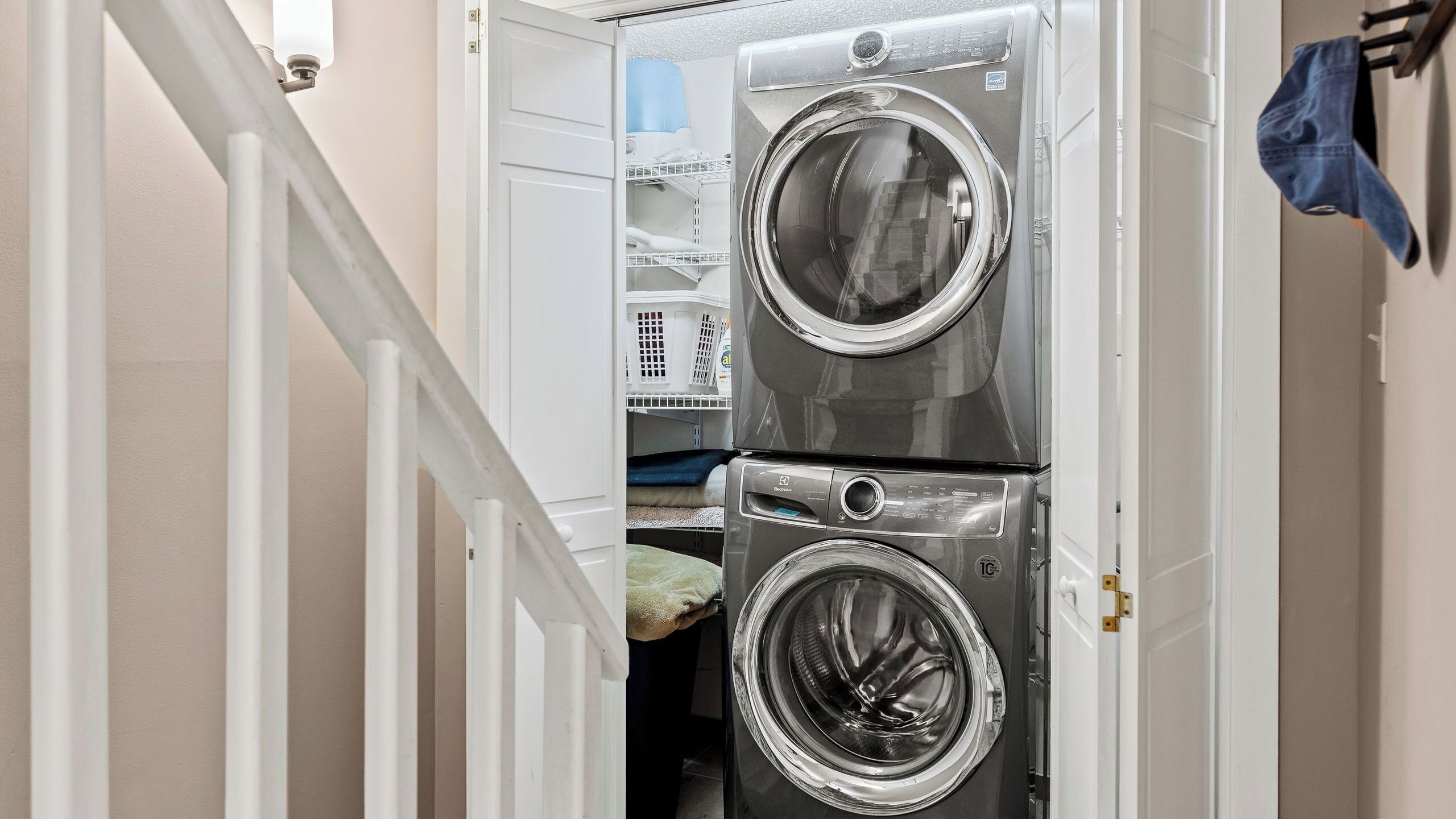 A laundry room with two stacked front-loading washing machines, a drying rack, and a blue towel hanging on the wall.