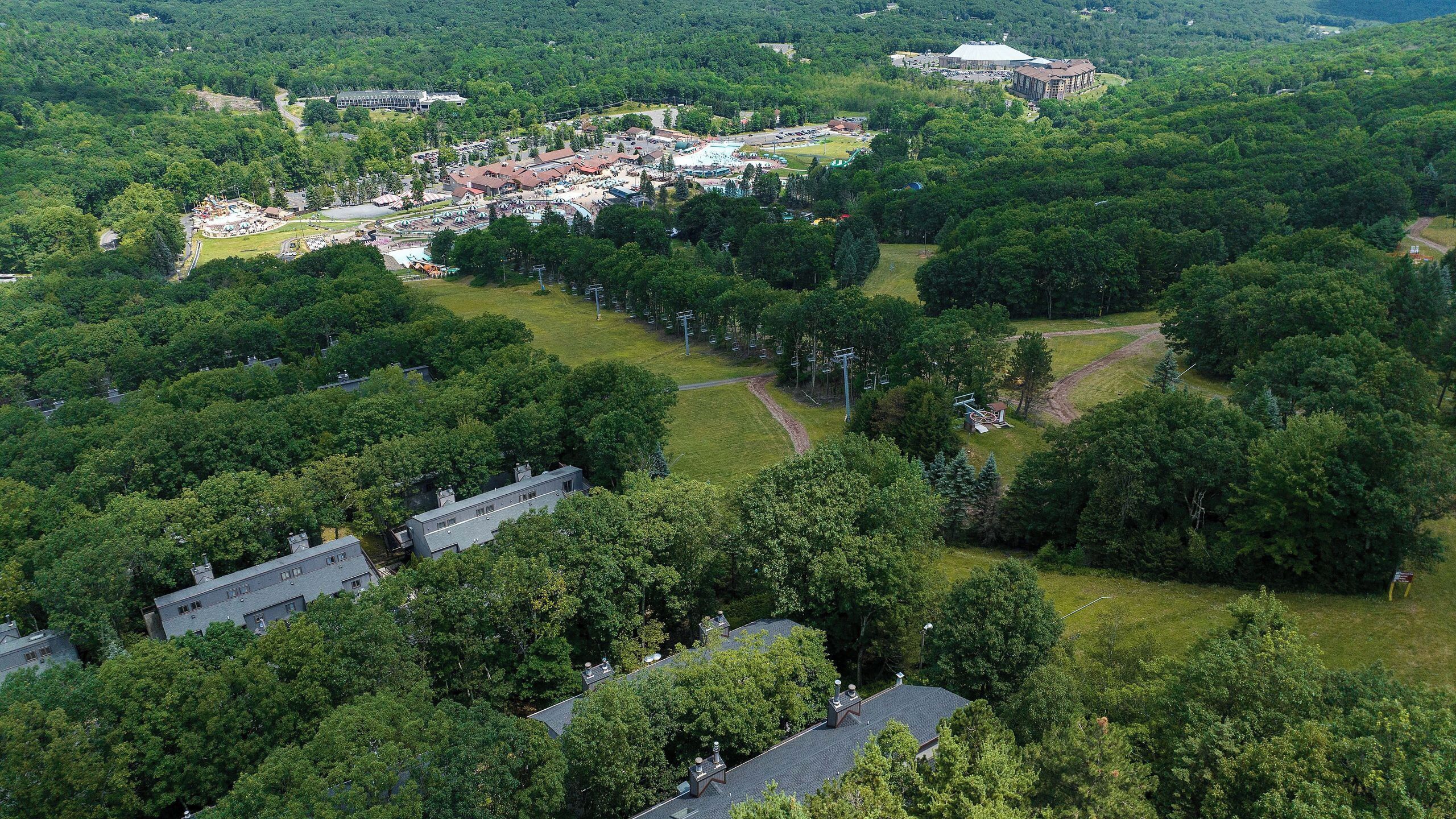 An aerial view of a resort area with multiple buildings, green spaces, and a large parking lot.