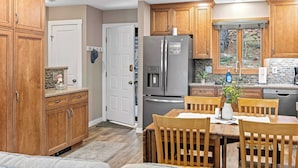 A modern kitchen with wooden cabinets, a stainless steel refrigerator, and a dining area with a table and chairs. - Alpine Escape by Avantstay On Camelback Mountain, Near Waterpark/attractions (Tannersville)