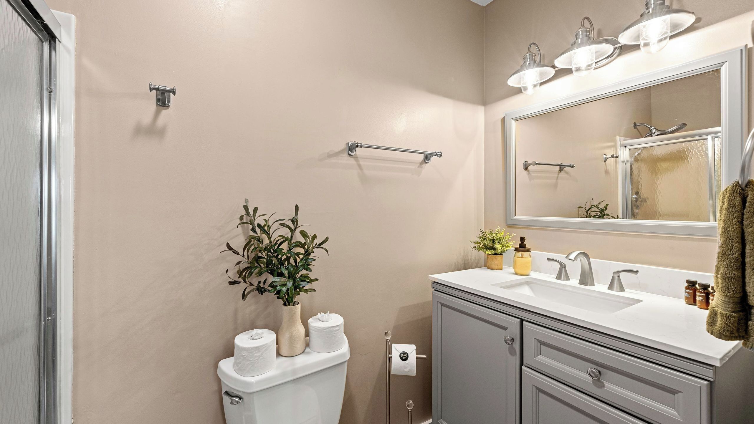 Une salle de bain équipée de toilettes, d’un lavabo, d’un miroir, d’un porte-serviettes et d’une plante.