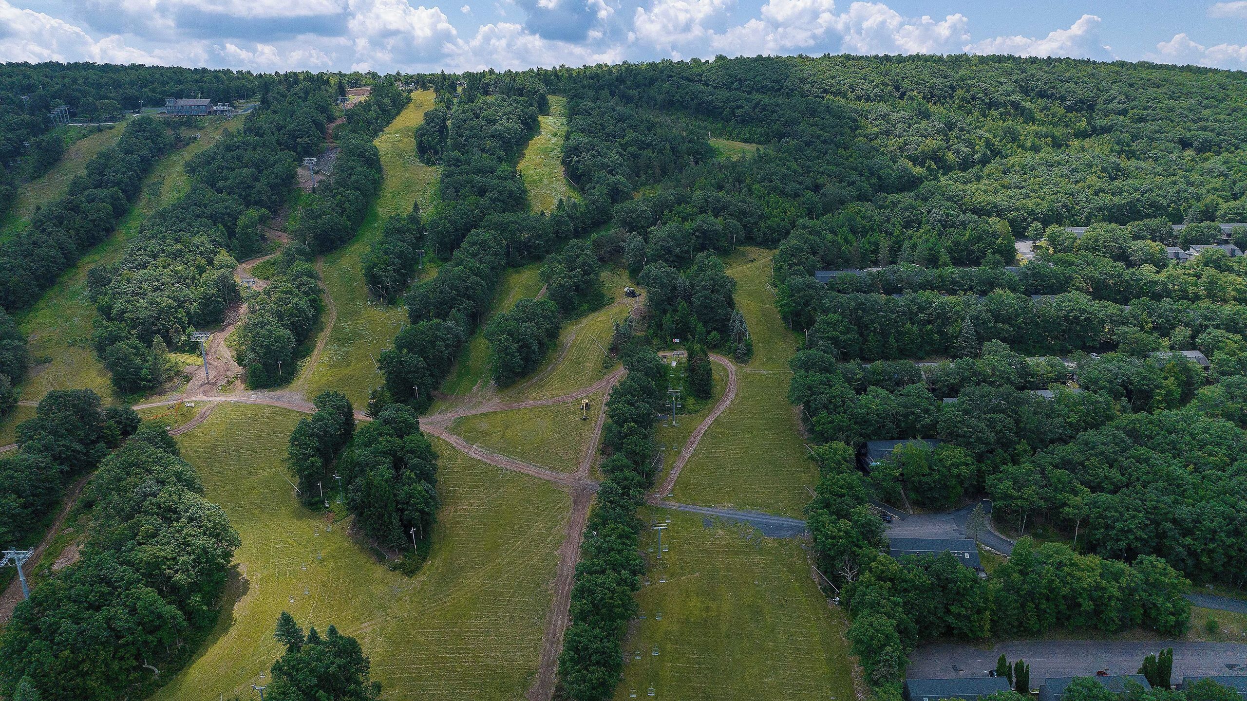 Eine Vogelperspektive auf eine hügelige Landschaft mit terrassierten Feldern, vereinzelten Bäumen und einigen Gebäuden.
