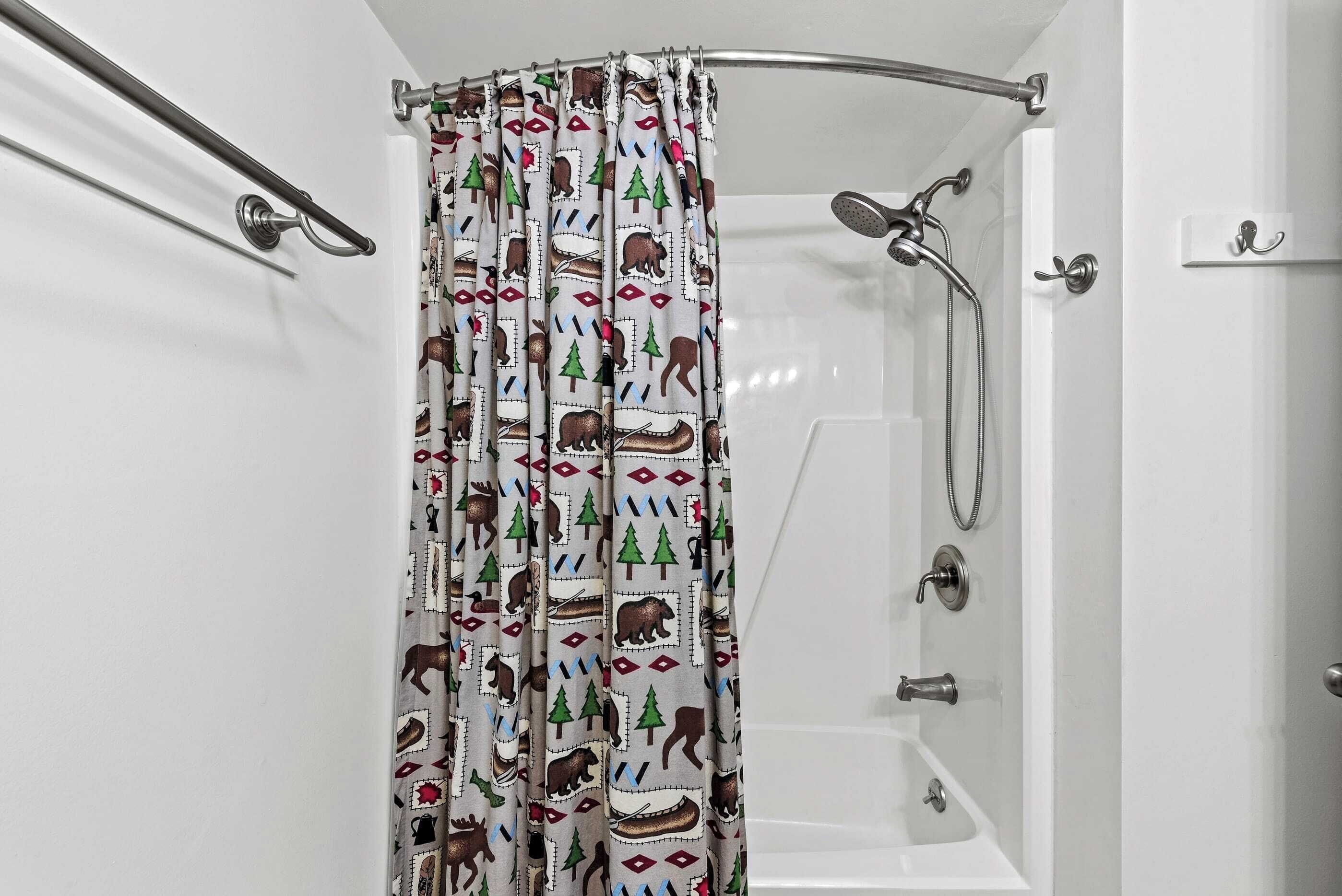 A bathroom with a shower curtain featuring a bear and tree pattern, a bathtub, and a handheld showerhead.