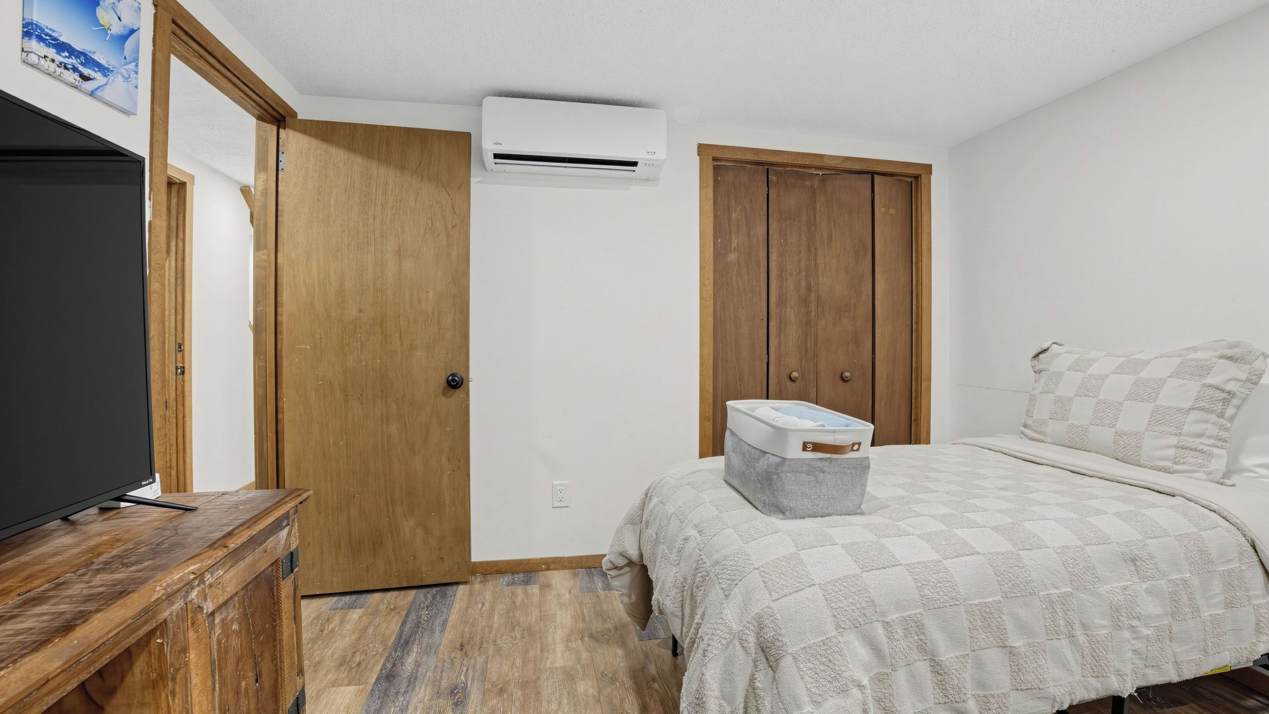 Een slaapkamer met een bed, een televisie op een houten standaard, een kledingkast en een airconditioning.