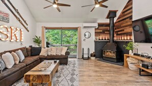 A cozy living room with a sofa, coffee table, and fireplace. There is a large window with a view of greenery outside. - Prime Location on Camelback Mtn, Renovated w/ Movie & Game Room The Bear's Den (Tannersville)