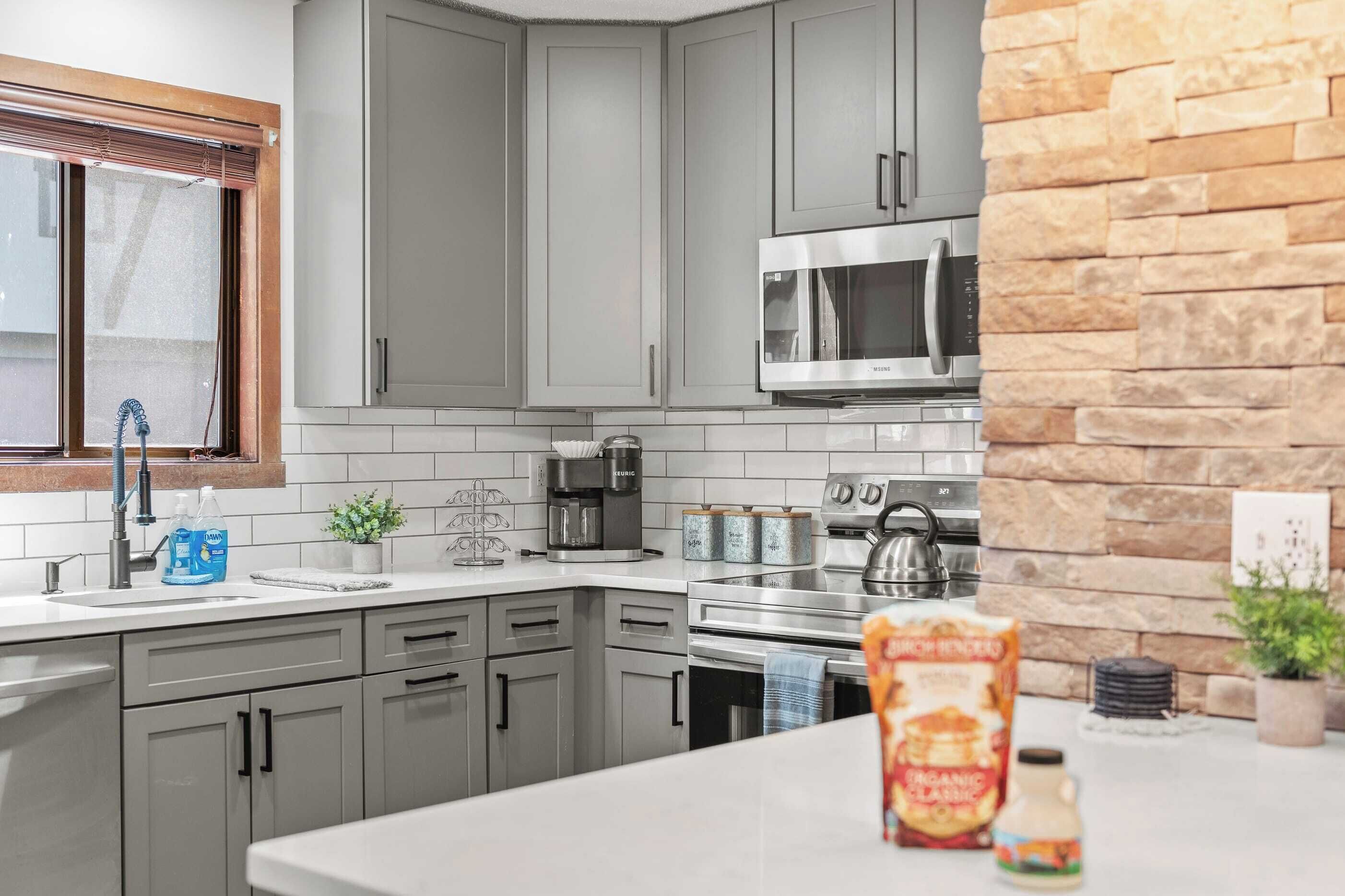 A modern kitchen with grey cabinets, a stainless steel microwave, a coffee maker, and a kettle.