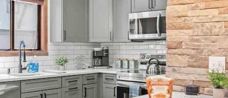 A modern kitchen with grey cabinets, a stainless steel microwave, a coffee maker, and a kettle.