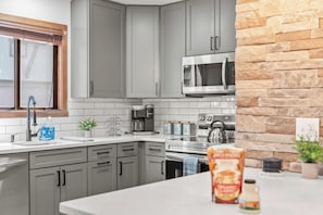 A modern kitchen with grey cabinets, a stainless steel microwave, a coffee maker, and a kettle.