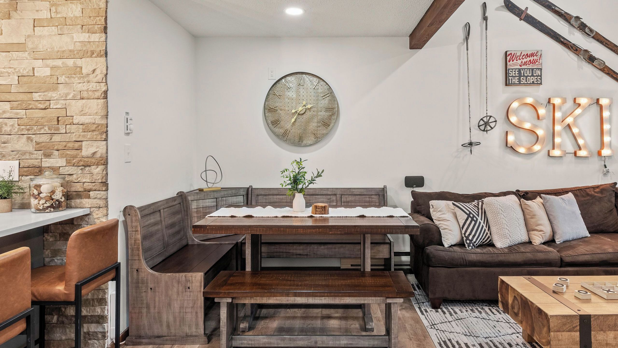 Ein gemütliches Zimmer mit Steinwand, einer Holzbank, einem Tisch, einem braunen Sofa und einer Wanduhr.