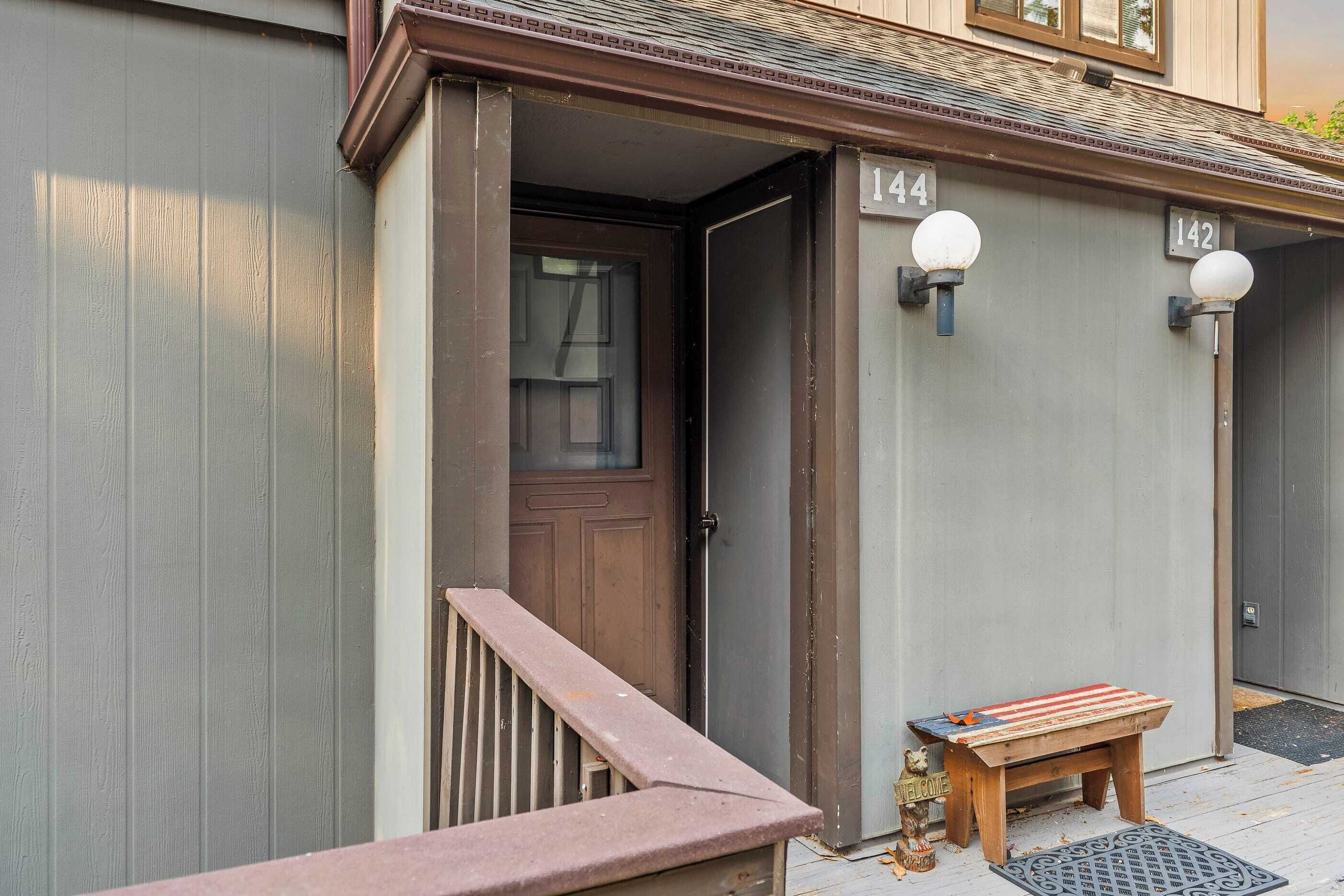 A building entrance with a brown door, a small wooden bench, and two wall-mounted light fixtures.