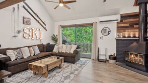 A cozy living room with a sectional sofa, a wooden coffee table, a fireplace, and a large window overlooking greenery. - Prime Location on Camelback Mtn, Renovated w/ Movie & Game Room The Bear's Den (Tannersville)