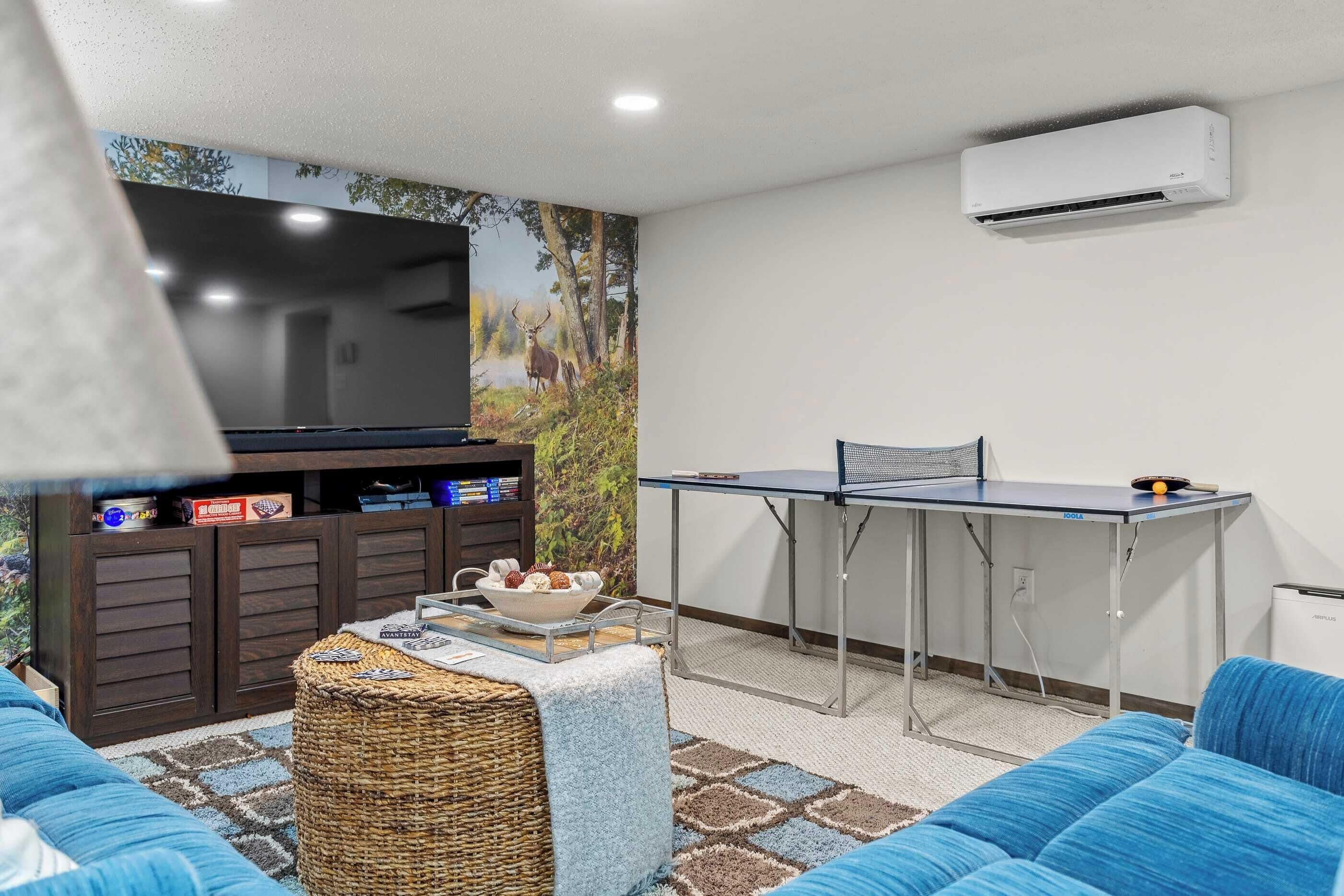 Uma sala de estar com televisão de tela plana, mesa de pingue-pongue e um sofá.
