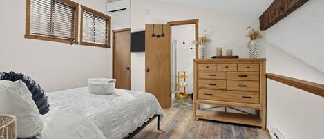 Una camera da letto con un letto, una cassettiera in legno e una porta che dà su un'altra stanza.