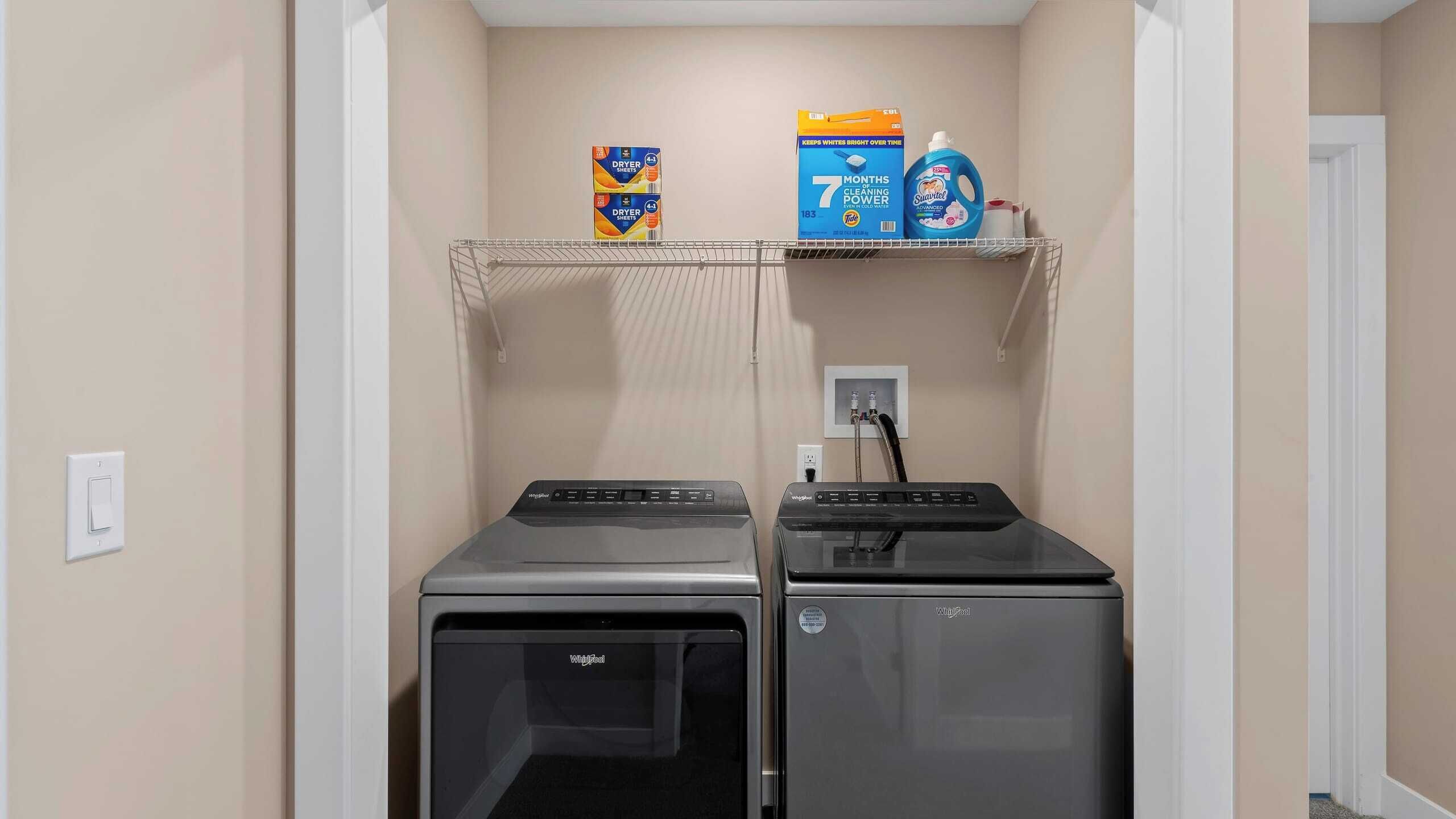 A laundry room with two front-loading washers and dryers, a shelf with laundry detergent, and a power outlet.