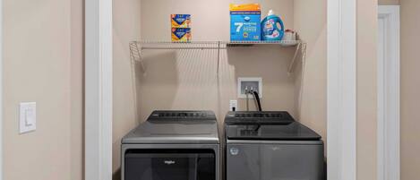 A laundry room with two front-loading washers and dryers, a shelf with laundry detergent, and a power outlet.