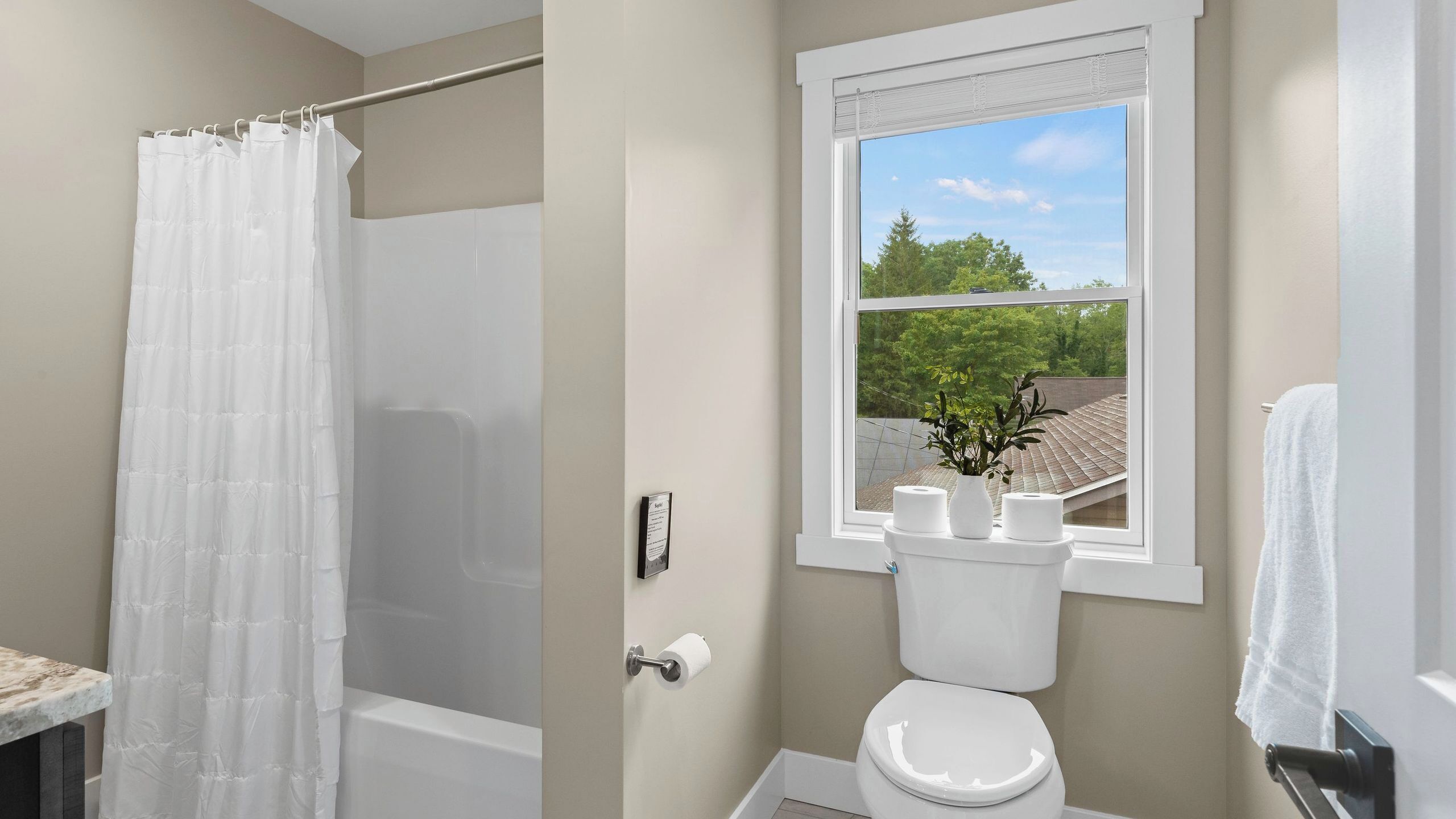A bathroom with a shower, toilet, and window with a view of trees and a building.