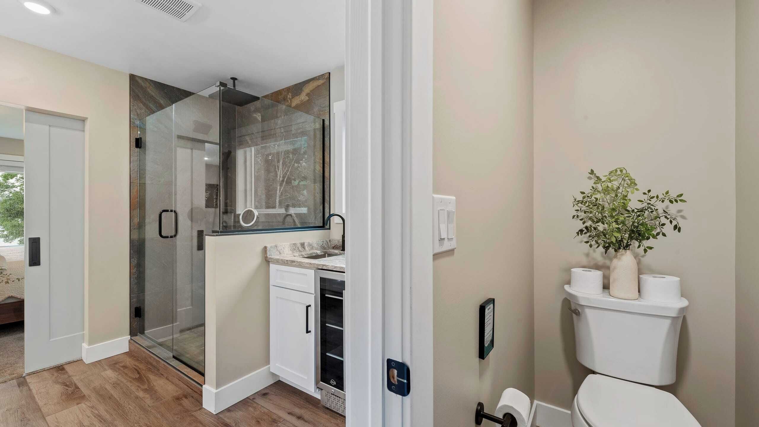 A modern bathroom with a glass shower enclosure, a toilet, and a sink with a marble countertop.