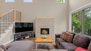 A modern living room with a flat-screen TV, a fireplace, a sofa, and a staircase. - Lakeside Serenity by Avantstay Lakefront, Newly Built, Deck w/ Views! (White Haven)