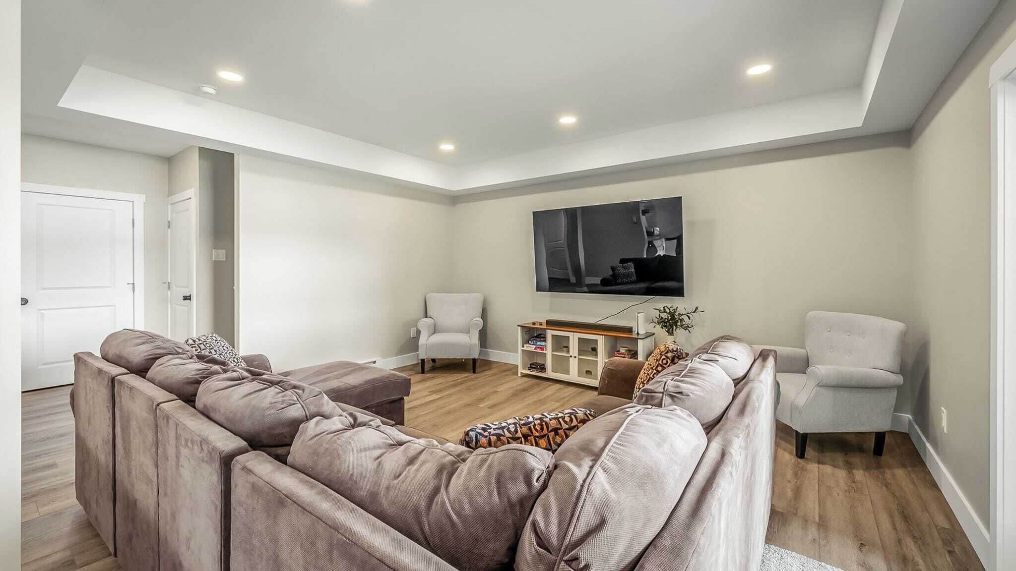 Una sala de estar moderna con un sofá modular, dos sillones, una mesa de centro y un televisor de pantalla plana montado en la pared.