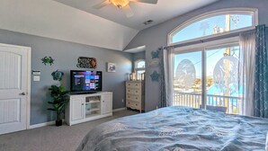 A bedroom with a bed, a television on a white cabinet, a ceiling fan, and a window with curtains. - Waves 'n Wooder by Avantstay Swimspa + Game Room, Walk to Beach (Wildwood)