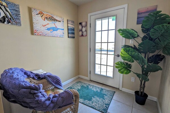 A hallway with a wicker chair, a purple blanket, a potted plant, and artwork on the walls.
