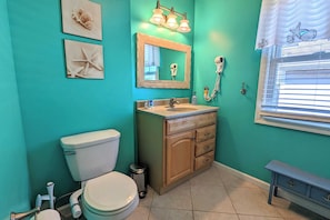 A bathroom with teal walls, a white toilet, a wooden vanity with a mirror, and a window with blinds. - Waves 'n Wooder by Avantstay Swimspa + Game Room, Walk to Beach (Wildwood)