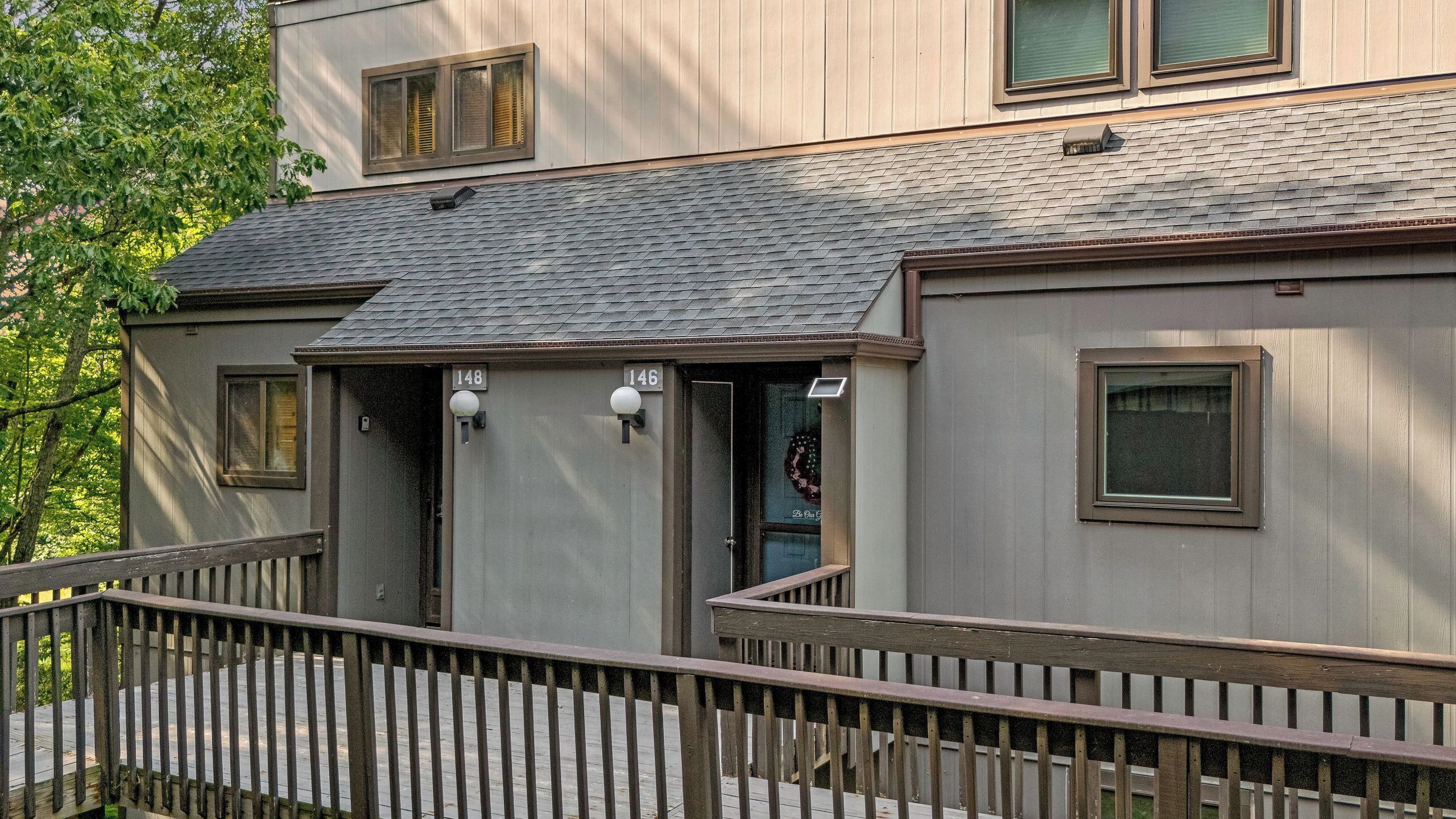 A two-story building with a grey exterior, a wooden deck, and a metal railing.