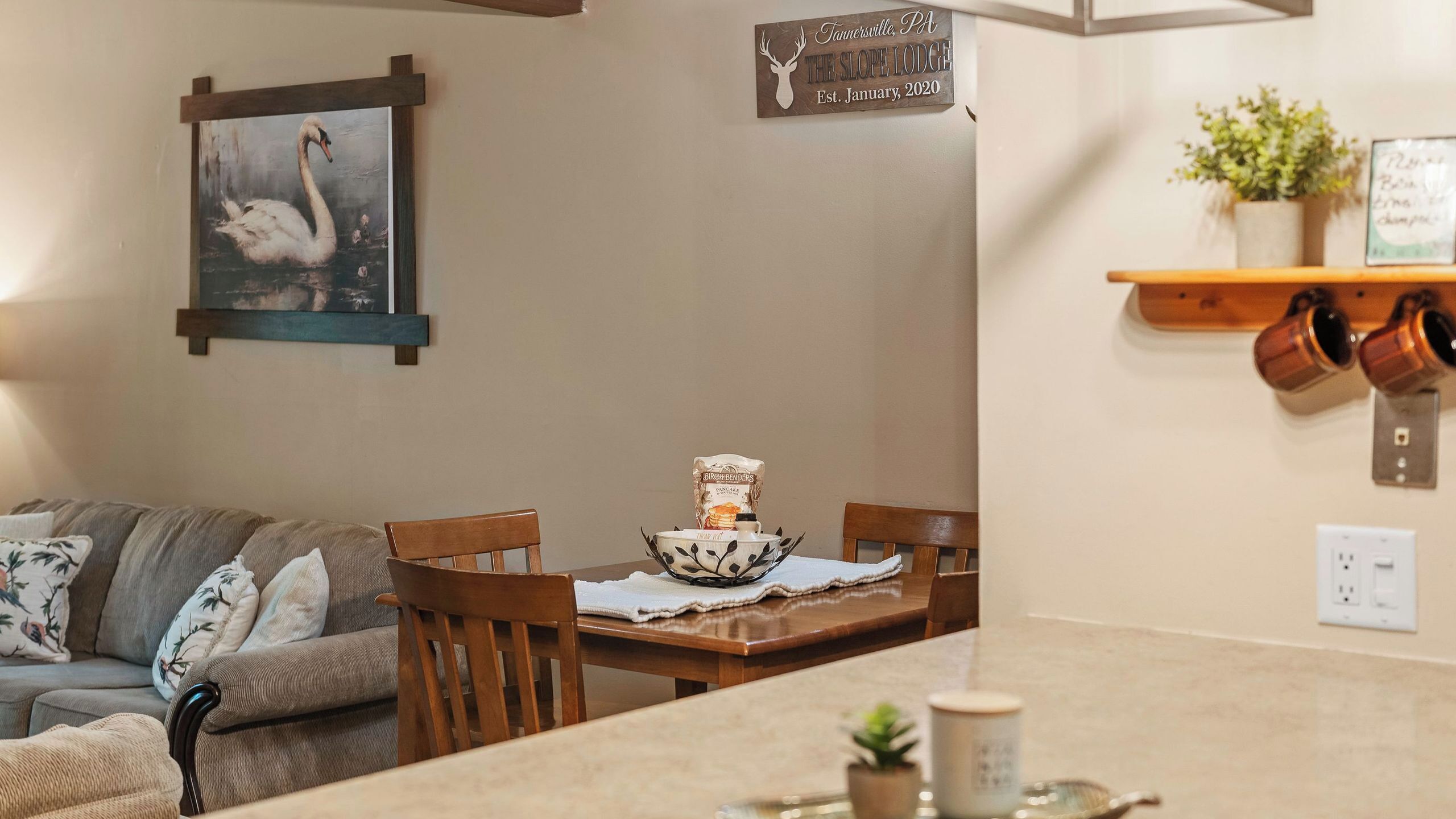 A dining area with a wooden table, chairs, a bowl of pancakes, and a sign indicating the establishment's name and date.
