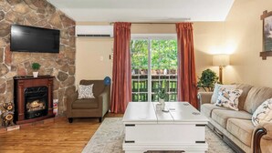 Una sala de estar con pared de piedra, chimenea, sofá, mesa de centro y televisor.