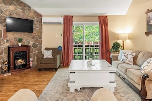 Una sala de estar con pared de piedra, chimenea, sofá, mesa de centro y televisor.