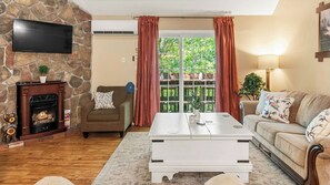 Una sala de estar con chimenea de piedra, un televisor de pantalla plana, un sofá, una mesa de centro y vistas a través de una puerta de cristal.