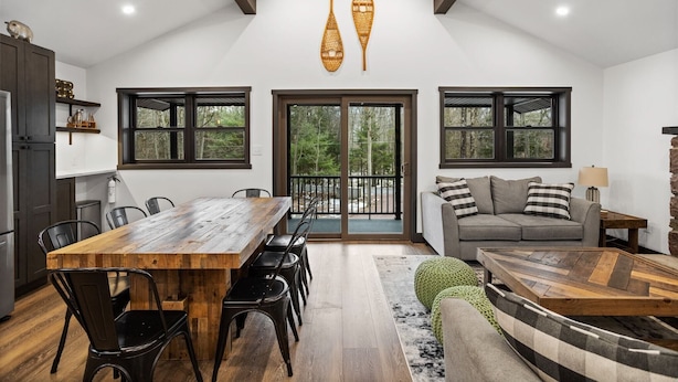 A spacious living area with a wooden dining table, black chairs, a grey sofa, and a patterned rug. - The Breck by Avantstay Modern 6bdr Cabin w/ Hot Tub & Game Room (Lake Harmony)