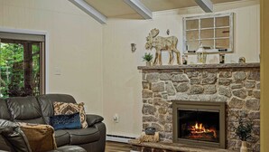 A cozy living room with a stone fireplace, a leather sofa, and a large window.