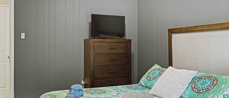 A bedroom with a bed, a dresser, and a television on top of it.