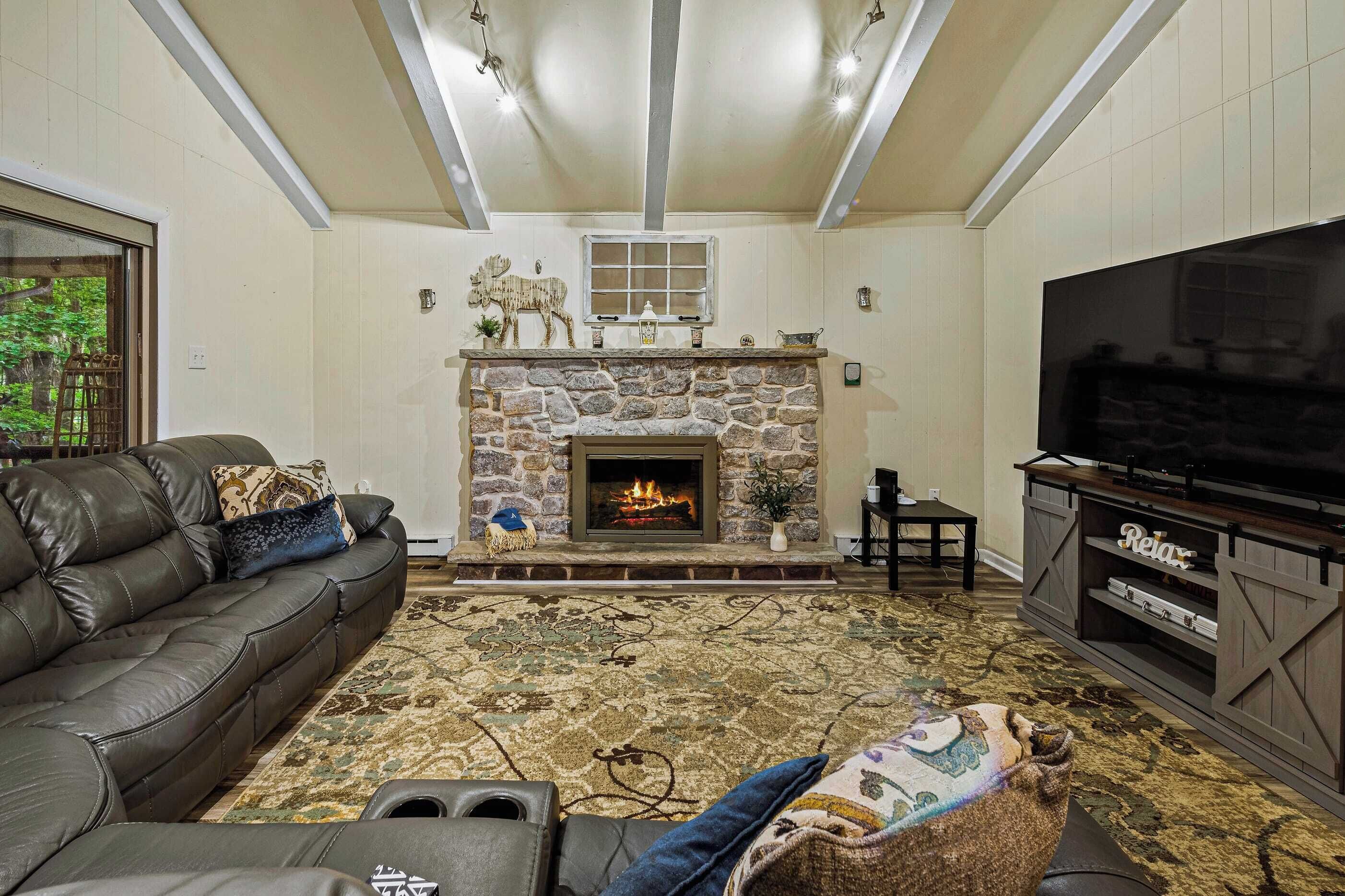 A living room with a stone fireplace, a leather sofa, a television, and a patterned rug.