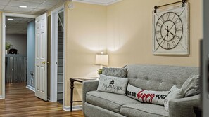 Una sala de estar con un sofá gris, un reloj de pared y una lámpara.